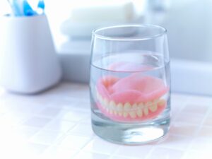 Set of dentures in a glass with clear fluid on a light tiled counter