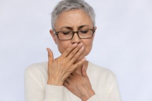 Woman in white sweater closing eyes holding her hand over her mouth