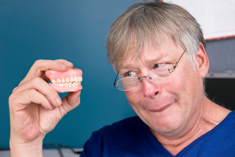 An older man looking at his dentures skeptically