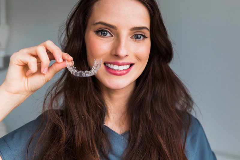 A young woman holding an Invisalign tray next to her face