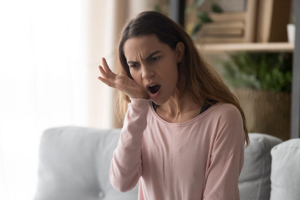 Woman on couch holding hand to jaw with mouth open in pain