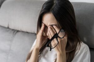 Woman holding her eyeglasses, struggling with eye pain