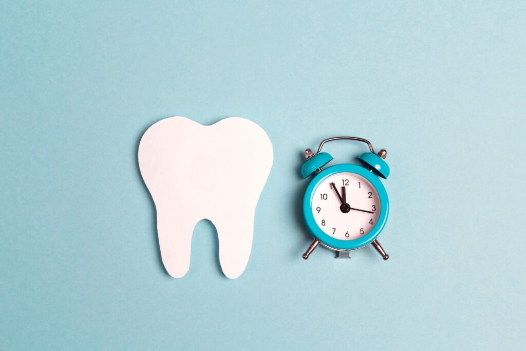 2D tooth next to teal alarm clock on teal background