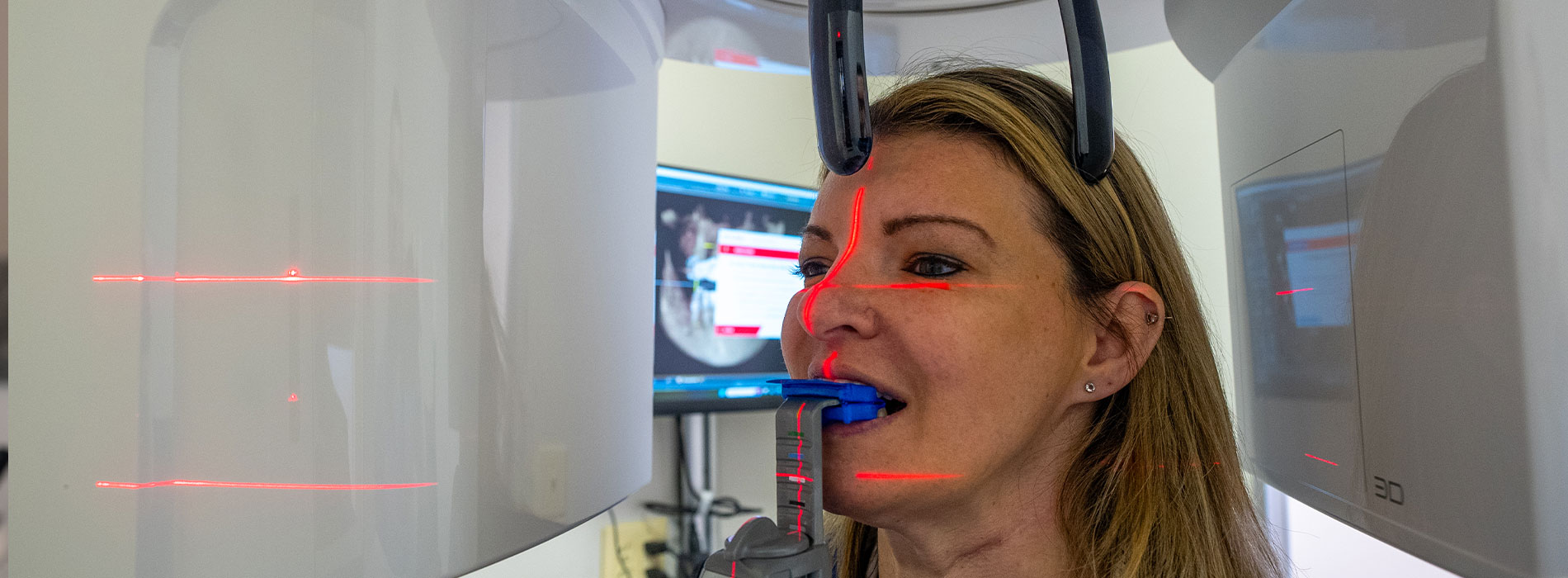 A person is seated in a dental chair, receiving care from a dental professional who stands behind them.